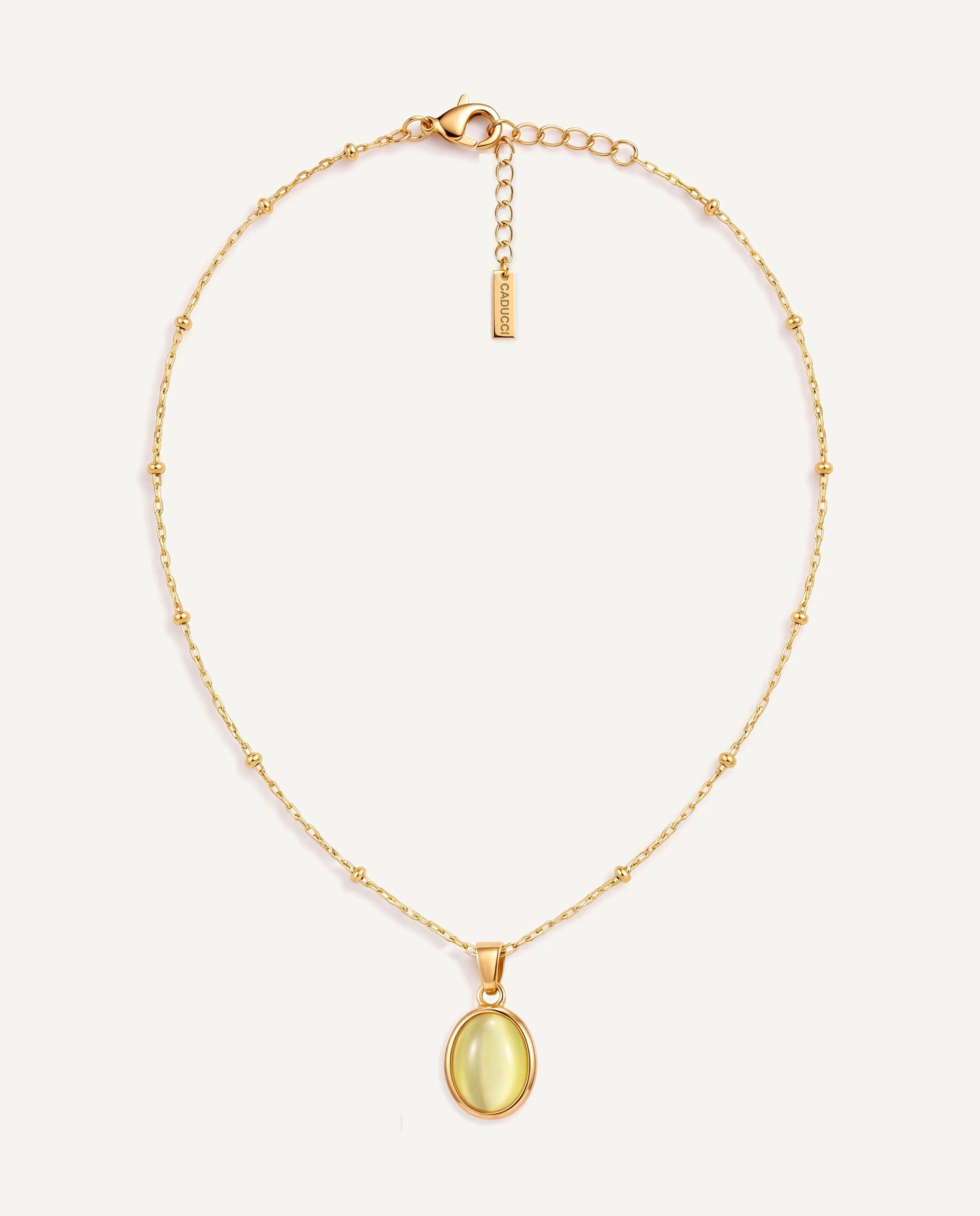 CADUCCI Capri Necklace in gold with an oval pale green cat's-eye pendant in a smooth bezel and a rectangular tag engraved with the CADUCCI logo