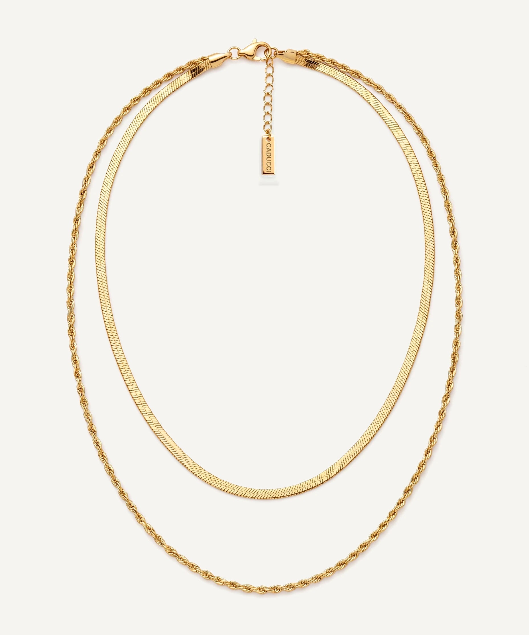 CADUCCI Firenze Necklace in gold, layered: a thin herringbone chain and a fine rope chain, with a rectangular tag engraved with the CADUCCI logo