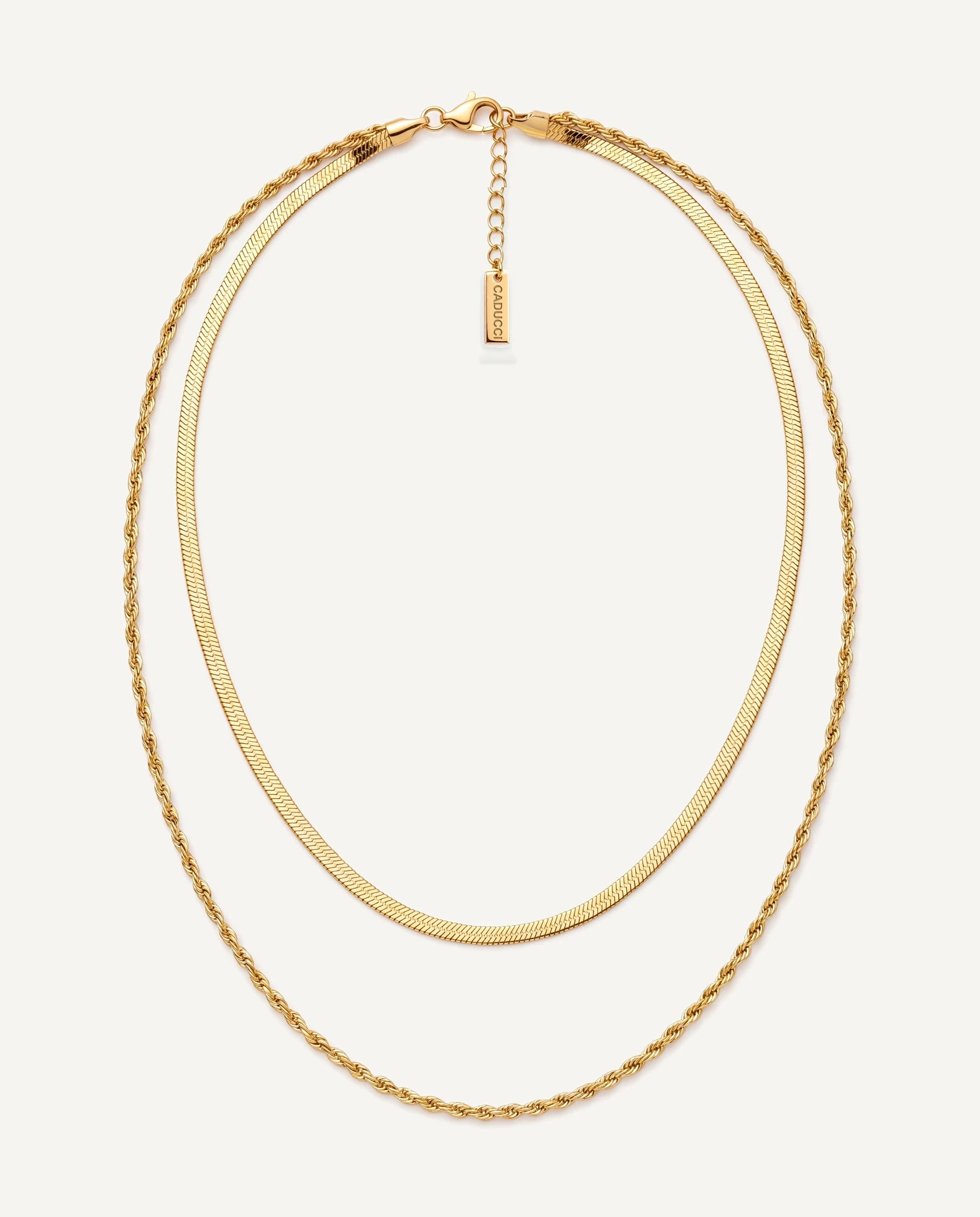 CADUCCI Firenze Necklace in gold, layered: a thin herringbone chain and a fine rope chain, with a rectangular tag engraved with the CADUCCI logo